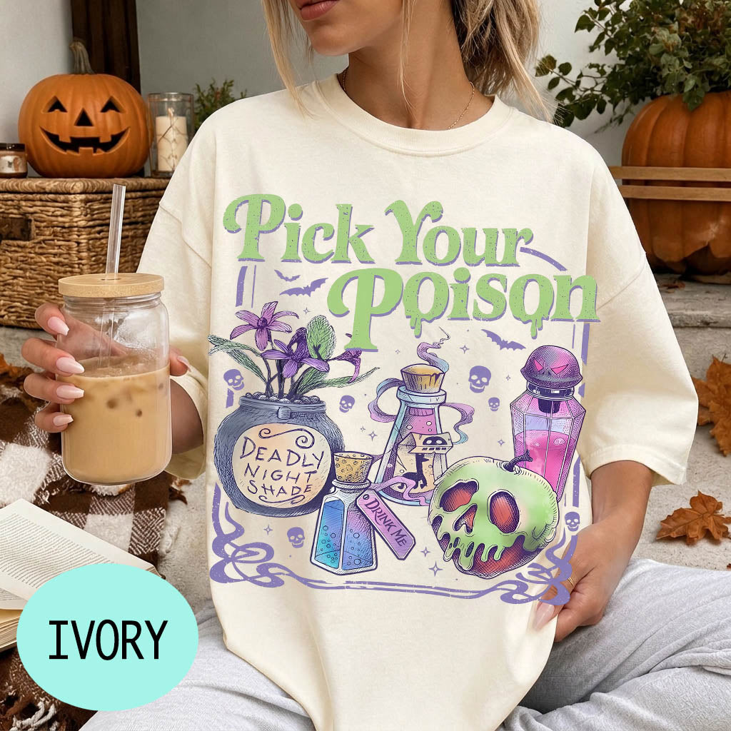 A woman wearing a white t-shirt with a graphic design featuring various Halloween-themed items, such as a skull, a vase, and a bottle, along with the text "Pick Your Poison". She is holding a drink in a glass with a straw.
