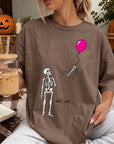 A woman wearing a t-shirt with a skeleton and a balloon graphic, holding a glass of iced coffee and a book.