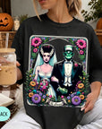 A woman wearing a black t-shirt with a graphic design featuring a bride and a Frankenstein monster, surrounded by flowers and a banner that says "The Lovers".