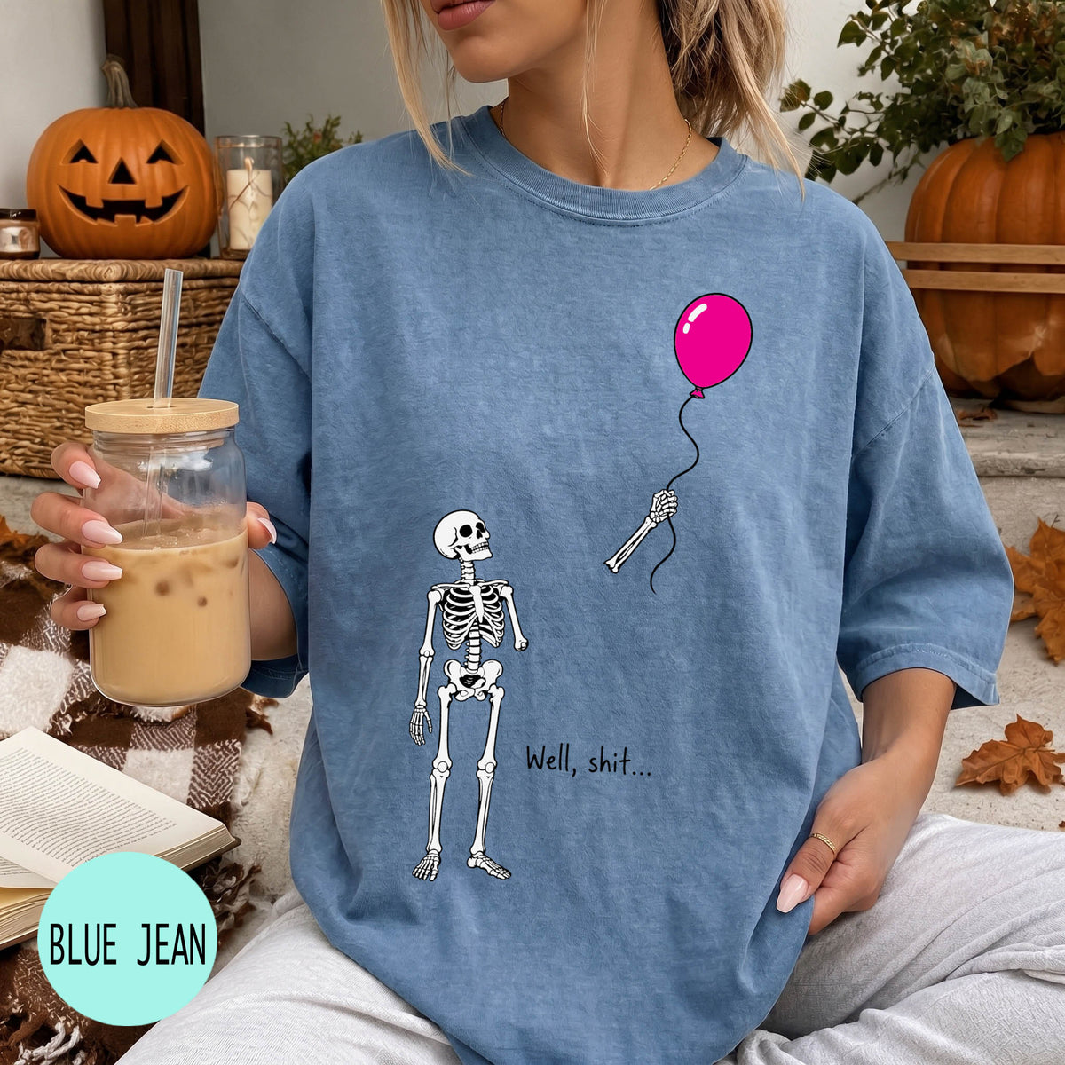 A woman wearing a blue t-shirt with a skeleton holding a pink balloon and the text "Well, shit..." printed on it.