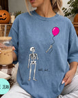 A woman wearing a blue t-shirt with a skeleton holding a pink balloon and the text "Well, shit..." printed on it.