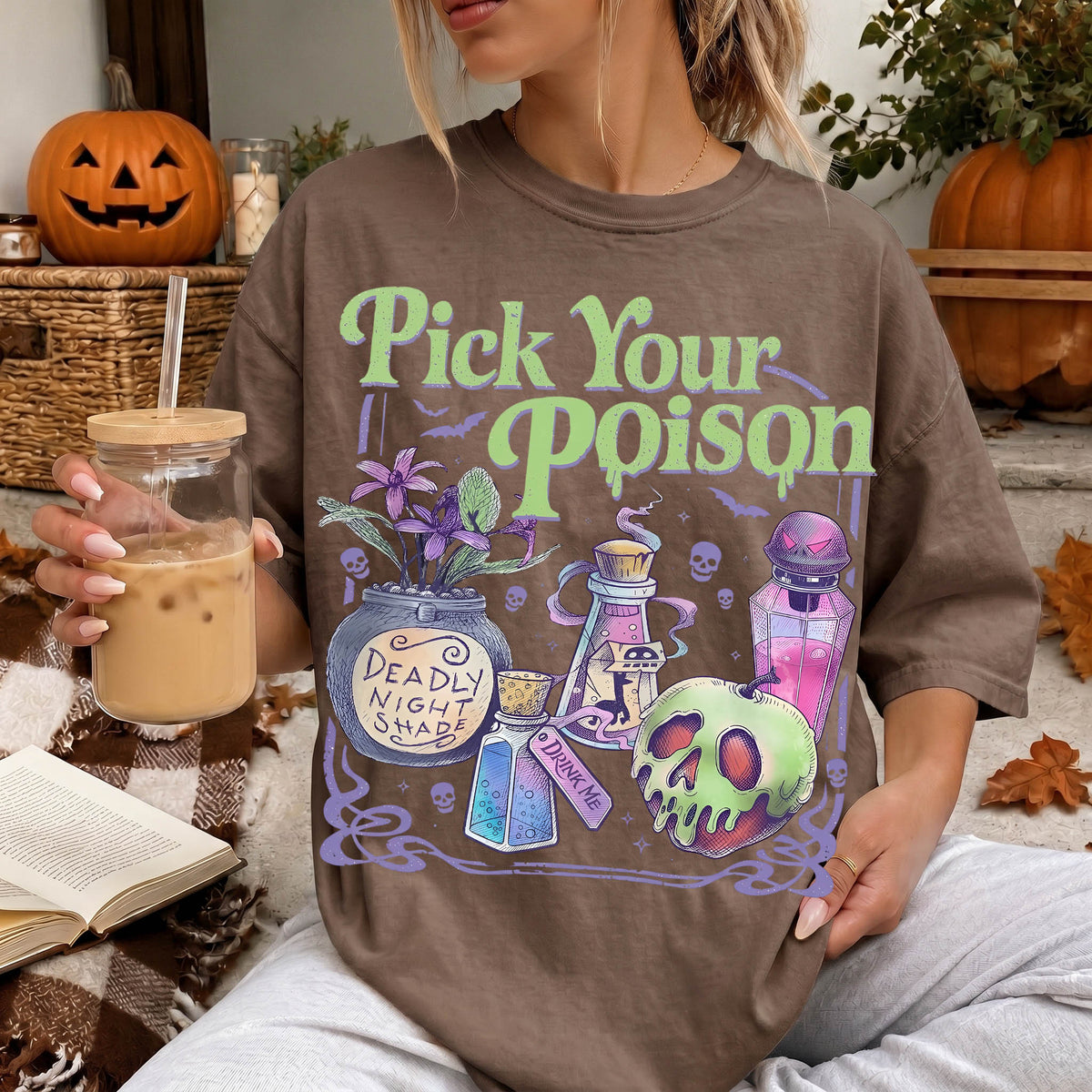A woman wearing a t-shirt with a Halloween-themed graphic and holding a drink, with a pumpkin and other Halloween decorations visible in the background.