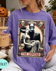 A woman wearing a purple t-shirt with a graphic design featuring a couple and the text "MONSTER THE LOVERS". She is holding a drink in her hand.