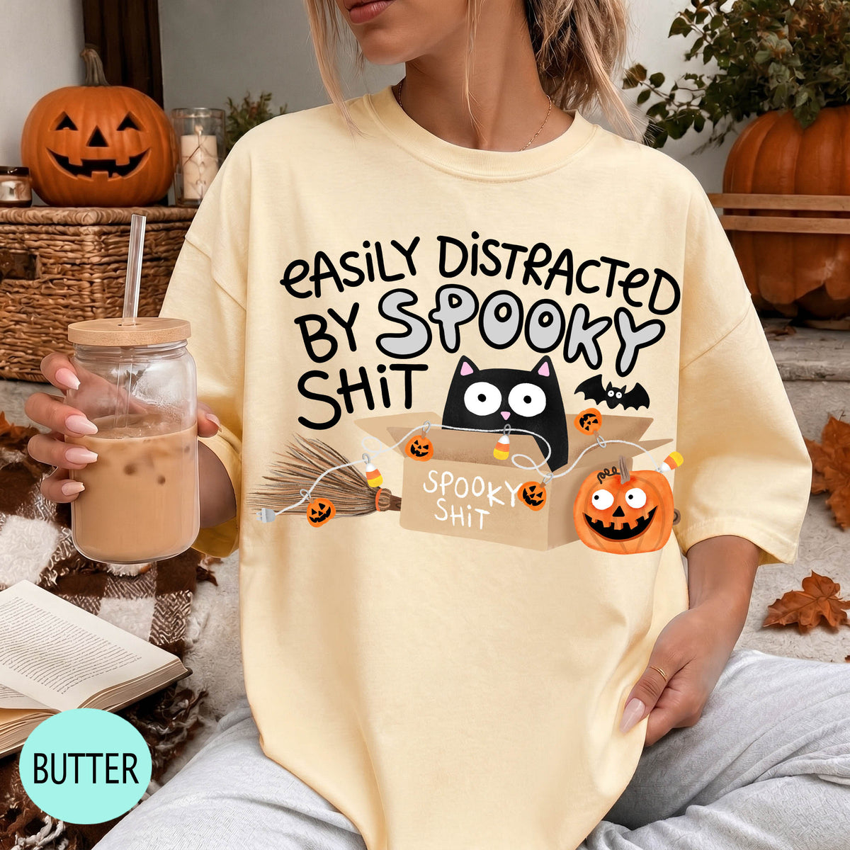 A person wearing a yellow t-shirt with a humorous Halloween-themed graphic, including a cat, pumpkin, and text that says "EASILY DISTracted BY SPOOKY SHIT".