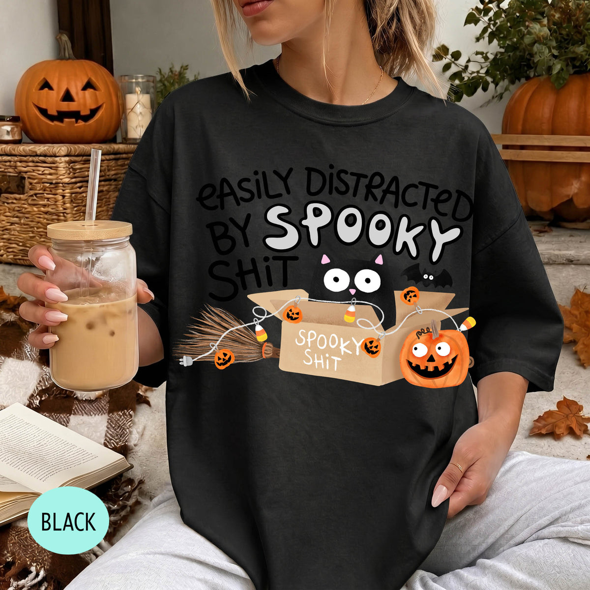 A person wearing a black t-shirt with a Halloween-themed graphic and text, holding a drink in a glass.