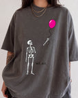 A person wearing a gray t-shirt with a graphic design depicting a skeleton holding a pink balloon.