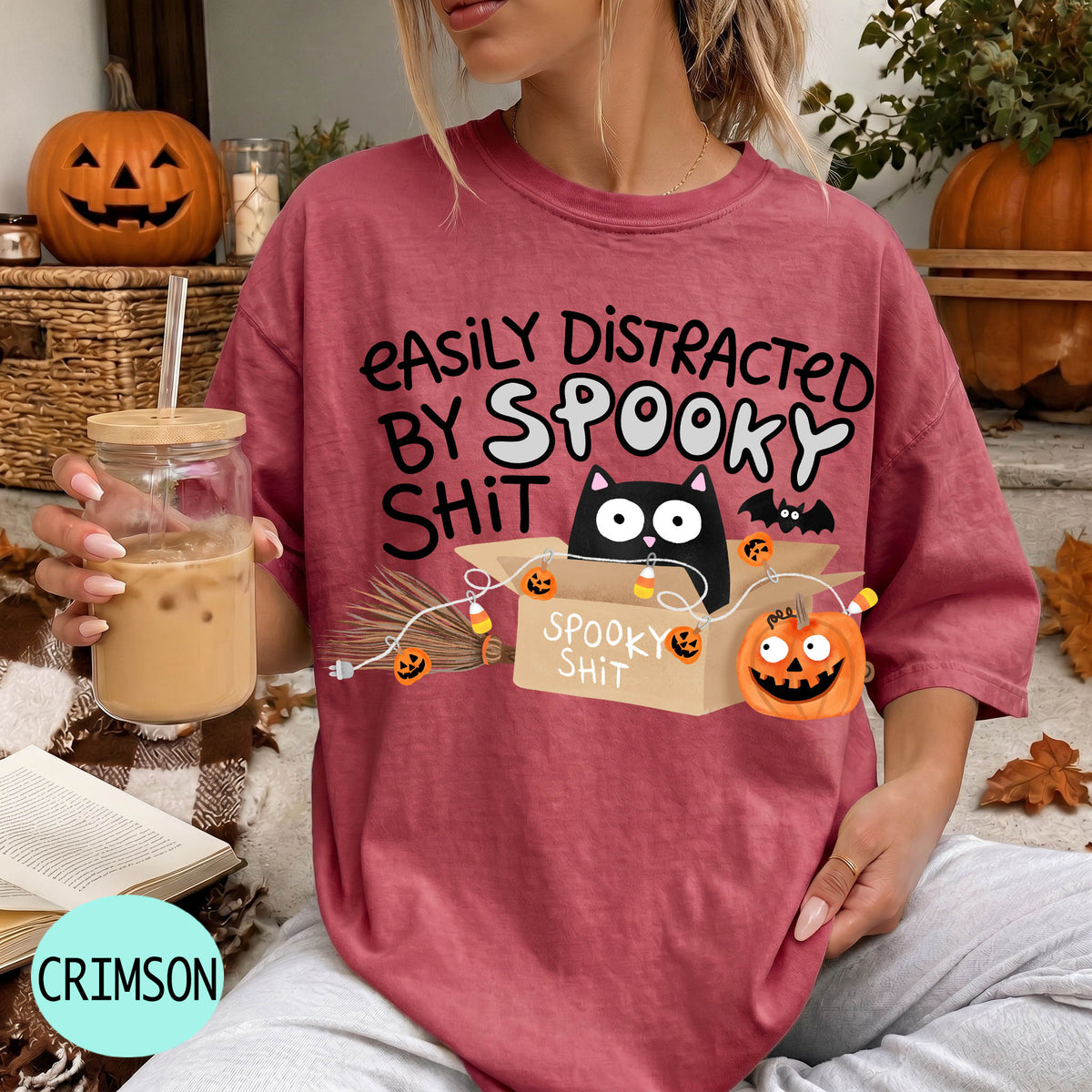 A woman wearing a red t-shirt with a Halloween-themed graphic and text, holding a drink in a glass.