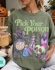 A woman wearing a green t-shirt with a Halloween-themed design, holding a drink and surrounded by Halloween decorations.