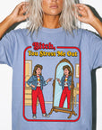 A woman with blonde hair wearing a blue t-shirt with a graphic design depicting a woman looking into a mirror and pointing at herself.