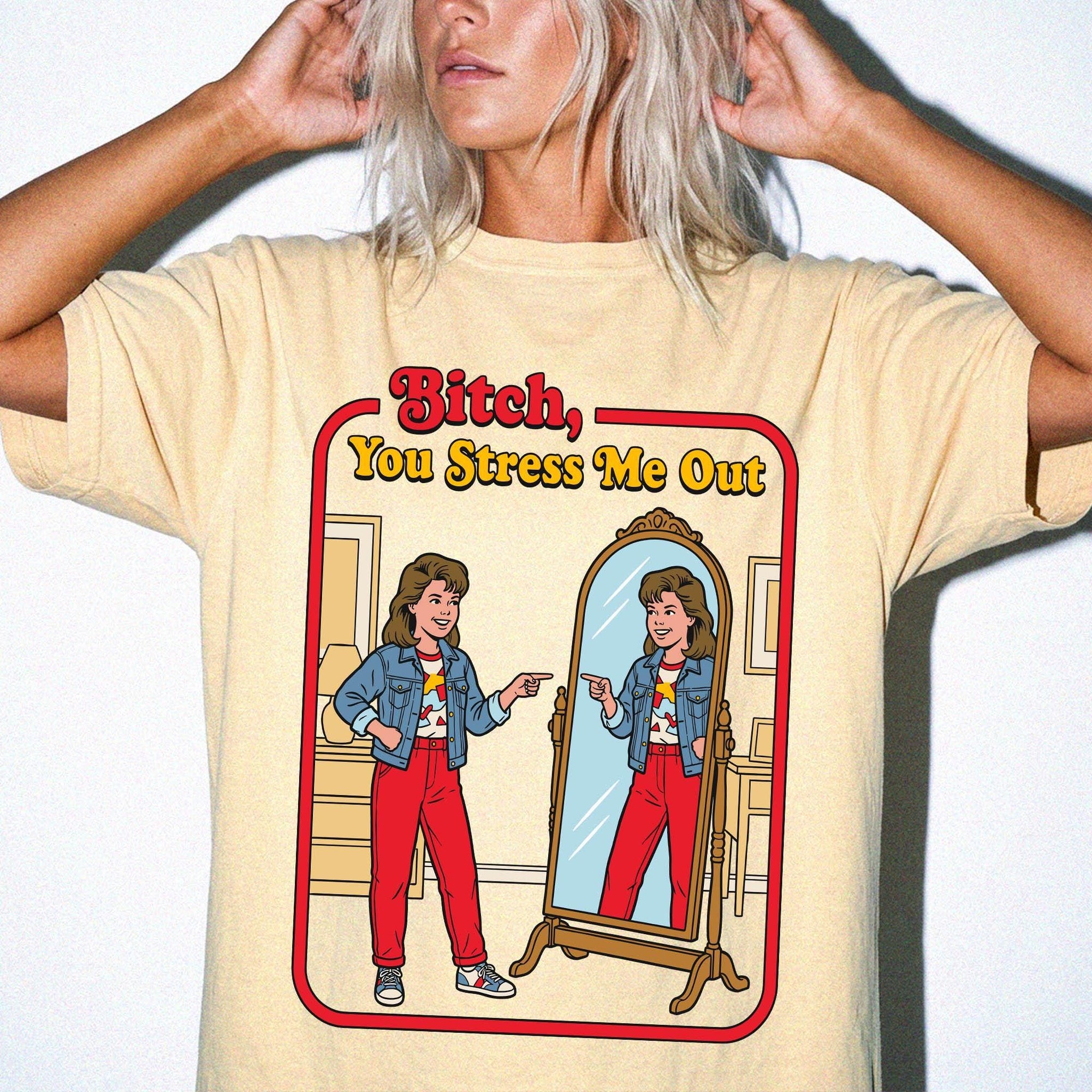 a woman wearing a yellow t-shirt with a graphic design depicting a woman looking into a mirror and pointing at herself.