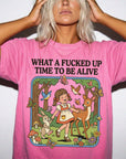 A woman wearing a pink t-shirt with a cartoon illustration of a girl interacting with a deer and other animals in a forest setting.
