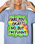 A person wearing a blue t-shirt with a colorful graphic and text that says "ARE YOU OKAY? NO, BUT I&