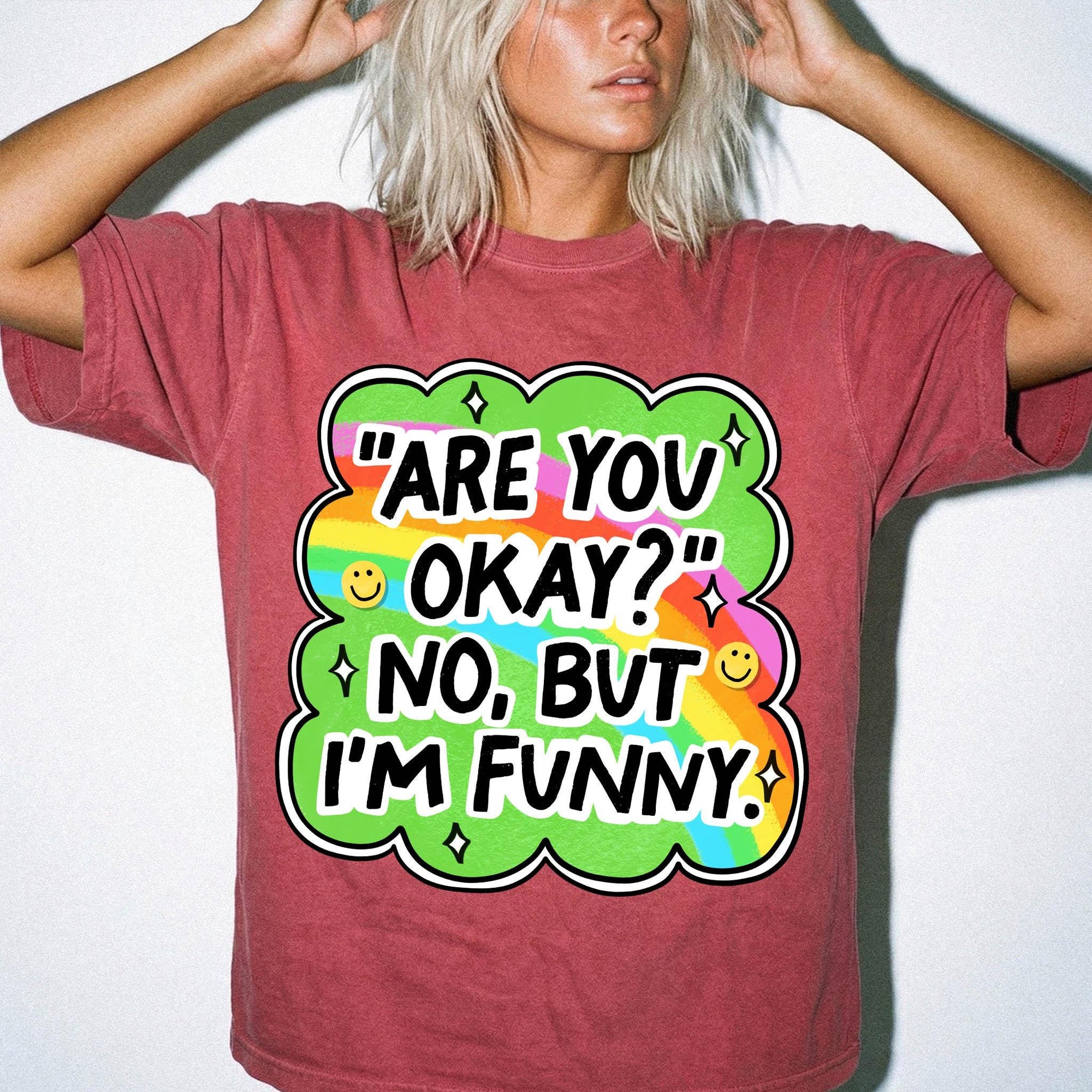 A person wearing a red t-shirt with a colorful graphic and text that says "ARE YOU OKAY? NO, BUT I'M FUNNY".