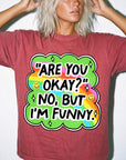 A person wearing a red t-shirt with a colorful graphic and text that says "ARE YOU OKAY? NO, BUT I&