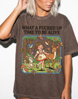 A woman wearing a t-shirt with a cartoon illustration of a girl and animals, including a deer, rabbit, and butterflies, along with the text "WHAT A FUCKED UP TIME TO BE ALIVE".