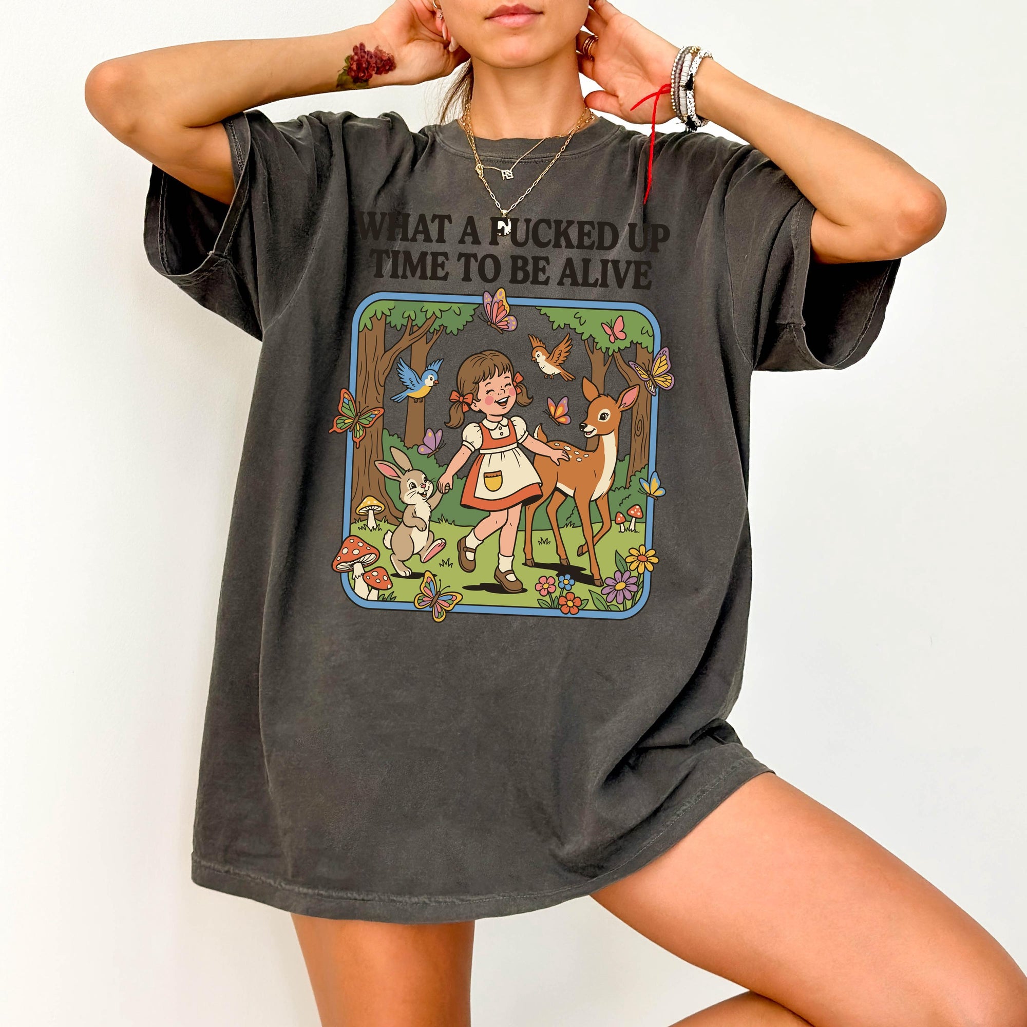 A person wearing a gray t-shirt with a graphic design depicting a young girl surrounded by various animals and elements, including a forest scene.