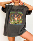 A person wearing a gray t-shirt with a graphic design depicting a young girl surrounded by various animals and elements, including a forest scene.