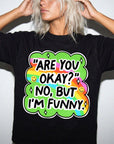 A person wearing a black t-shirt with a colorful graphic design and text that says "ARE YOU OKAY? NO, BUT I&