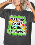 A woman wearing a gray t-shirt with a colorful graphic and text that says "ARE YOU OKAY? NO, BUT I&