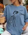 A woman wearing a blue t-shirt with a skeleton drawing and the word "boop" printed on it, holding a glass of iced coffee.