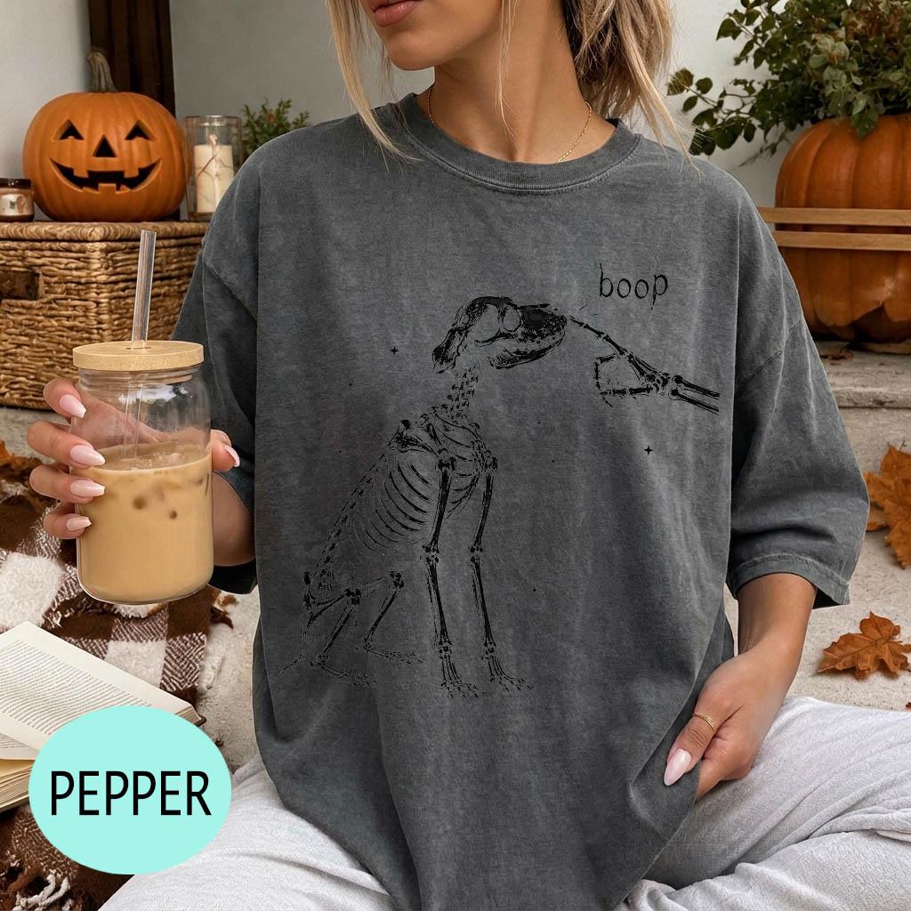 A woman wearing a gray t-shirt with a skeleton drawing and the word &amp;quot;boop&amp;quot; printed on it, holding a glass of iced coffee.