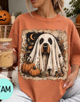 A woman is sitting on a couch, wearing a t-shirt with a Halloween-themed graphic of a ghost dog. She is holding a drink in a glass with a straw.