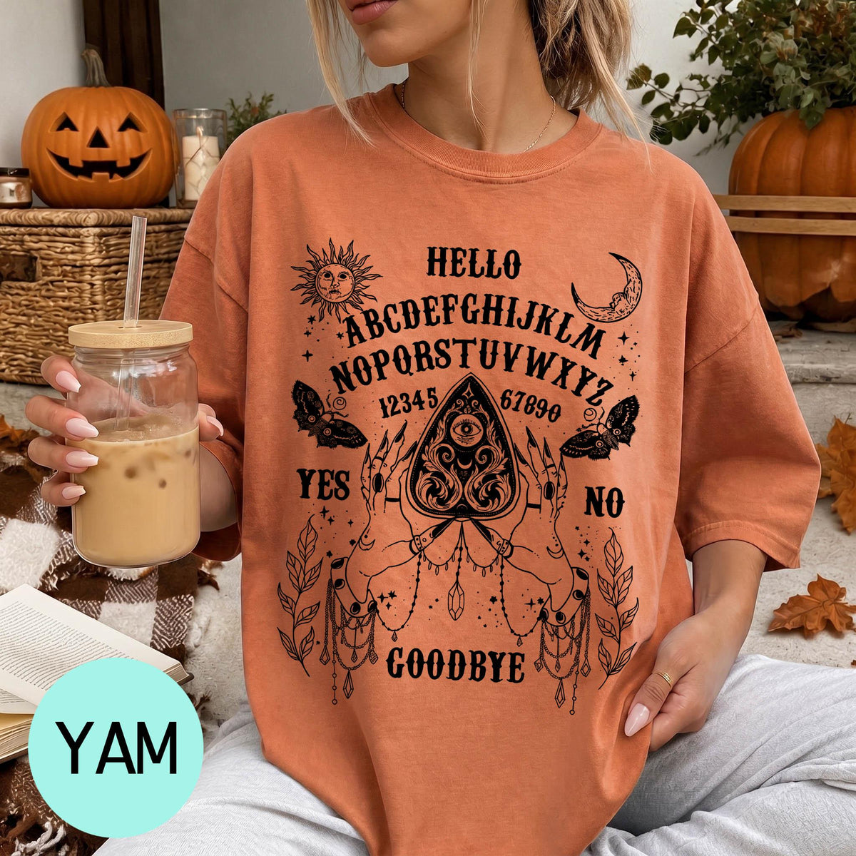A woman wearing an orange t-shirt with a Ouija board design and text printed on it, holding a drink in a glass.