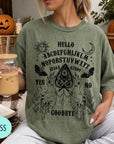 A woman wearing a green t-shirt with an Ouija board design and text printed on it, holding a drink in a glass.