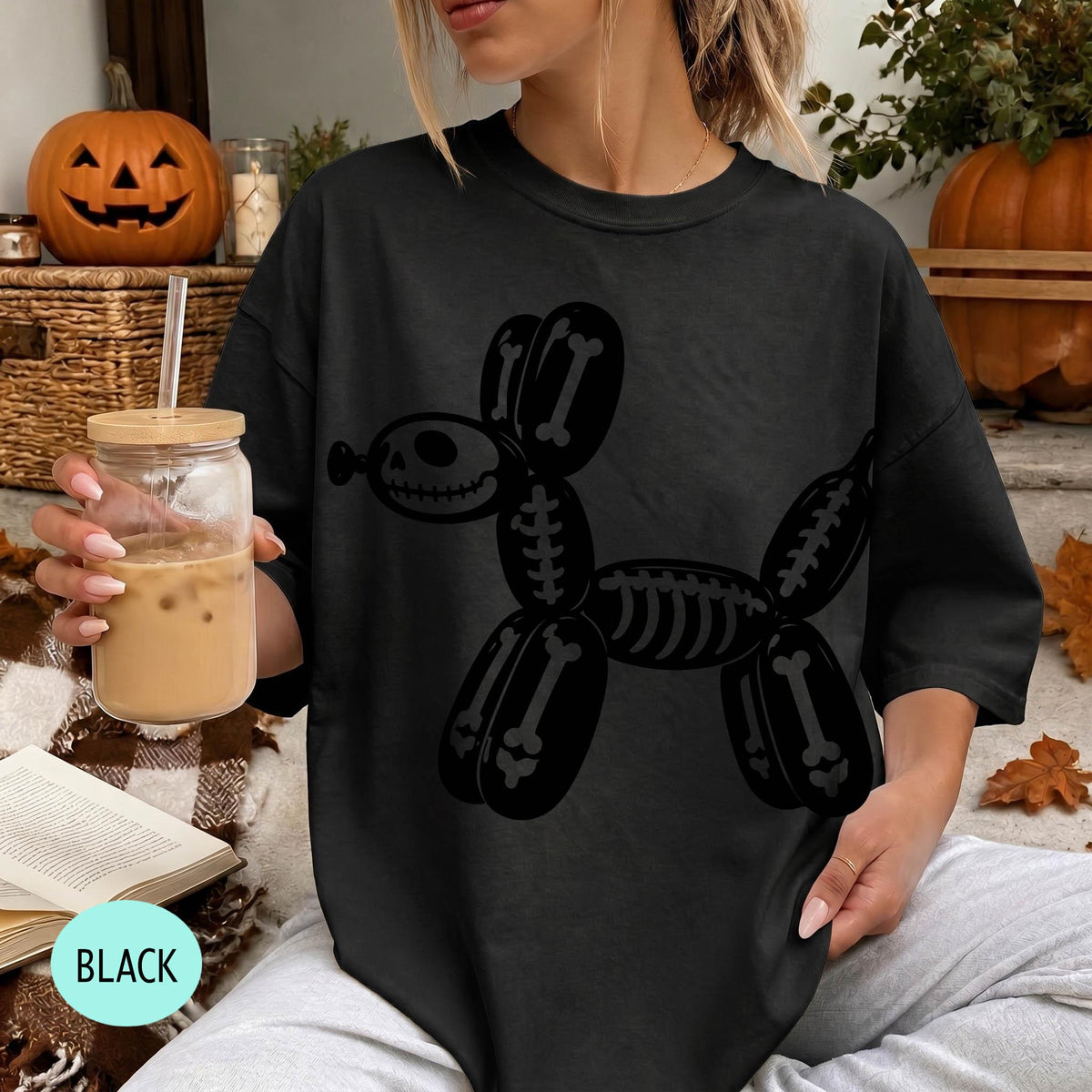 A woman wearing a black t-shirt with a skeleton dog design is sitting on a couch, holding a drink in a glass with a straw.