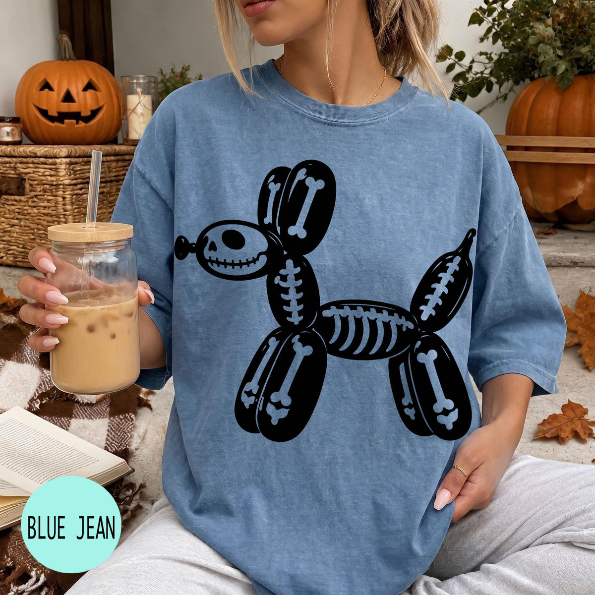 A woman wearing a blue t-shirt with a skeleton dog graphic is sitting on a couch, holding a drink in a glass.