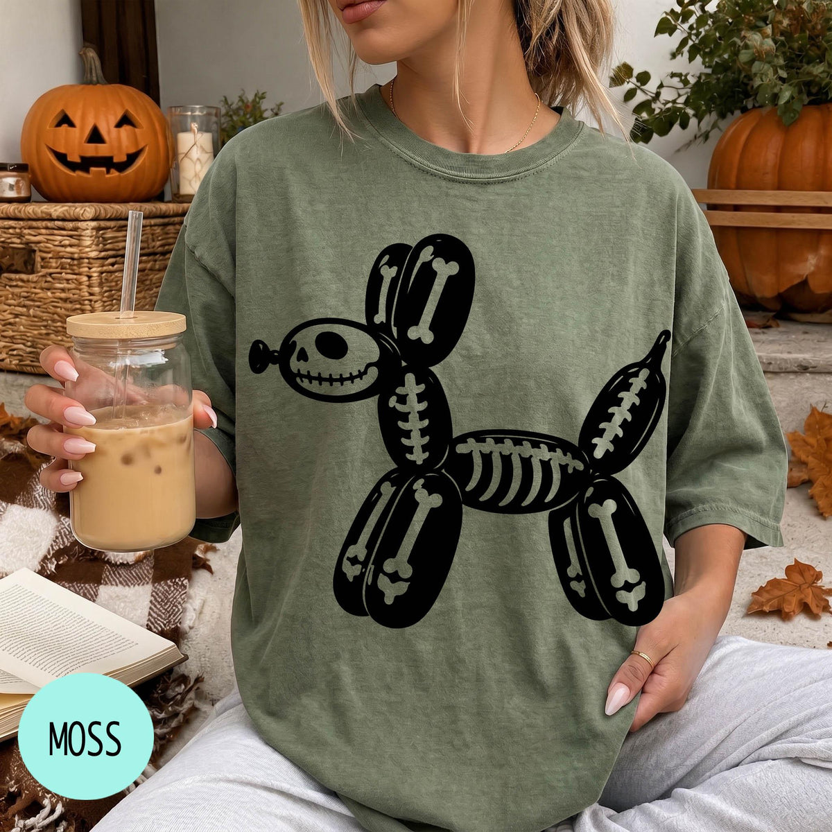 A woman wearing a green t-shirt with a skeleton dog graphic is sitting on a couch, holding a drink in a glass.