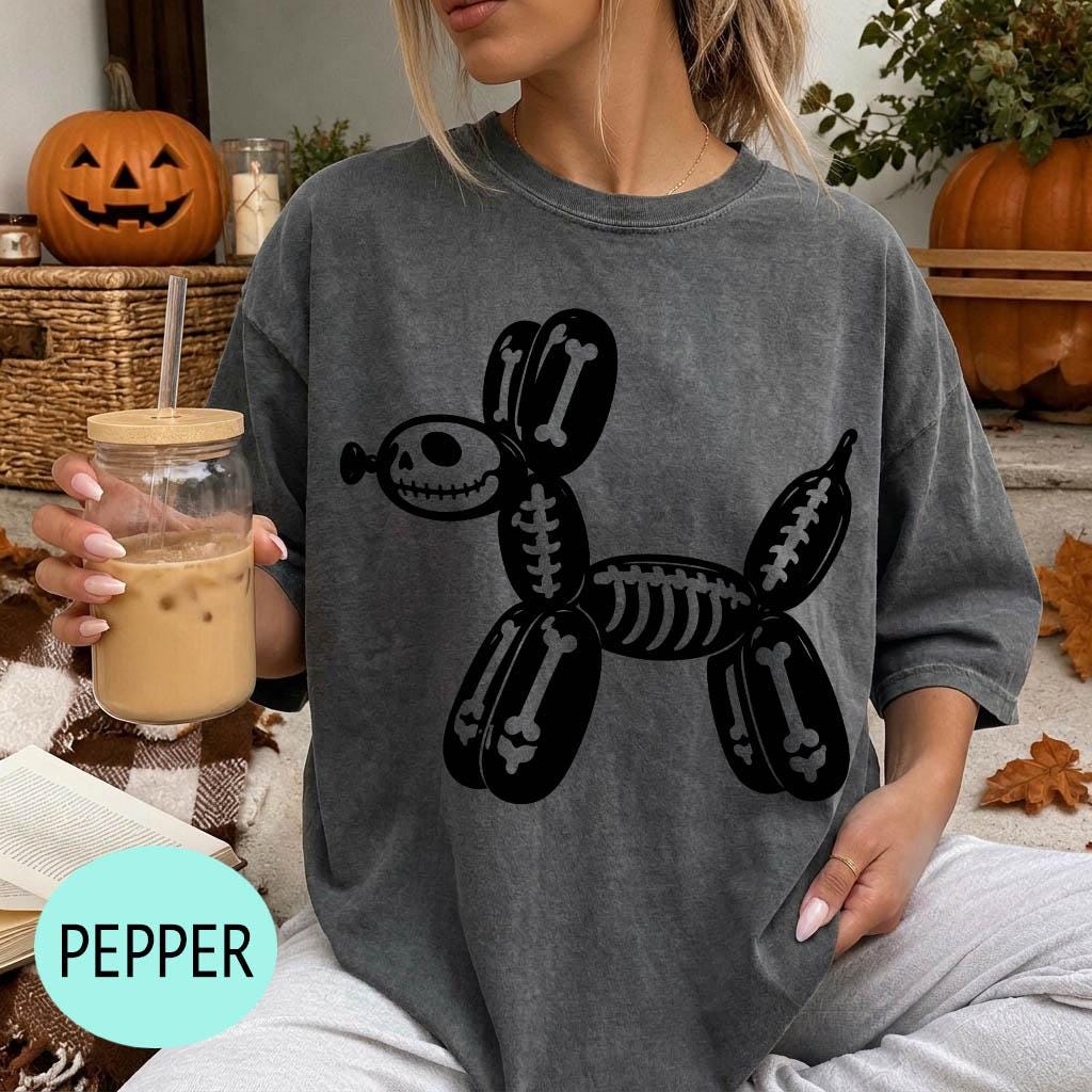 A woman wearing a gray t-shirt with a skeleton dog graphic is sitting on a couch, holding a drink in a glass.