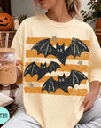 A woman wearing a yellow t-shirt with a graphic of bats and stars is sitting on a couch, holding a drink in a glass.