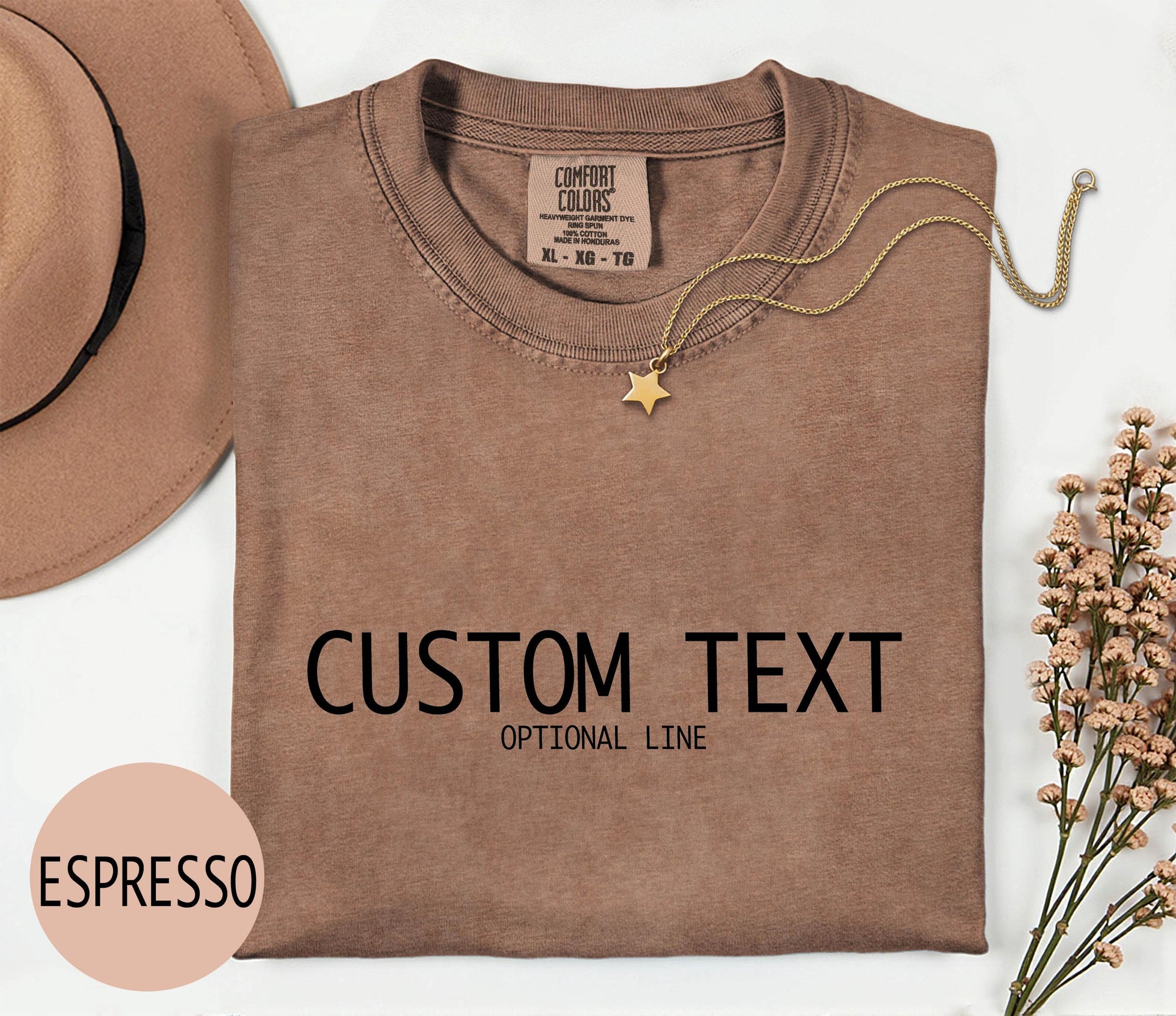 a brown t-shirt with the text &amp;quot;CUSTOM TEXT&amp;quot; printed on it, along with the word &amp;quot;OPTIONAL LINE&amp;quot;. The t-shirt is displayed on a white background, accompanied by a hat, a necklace, and some flowers. The word &amp;quot;ESPRESSO&amp;quot; is also visible in the image.