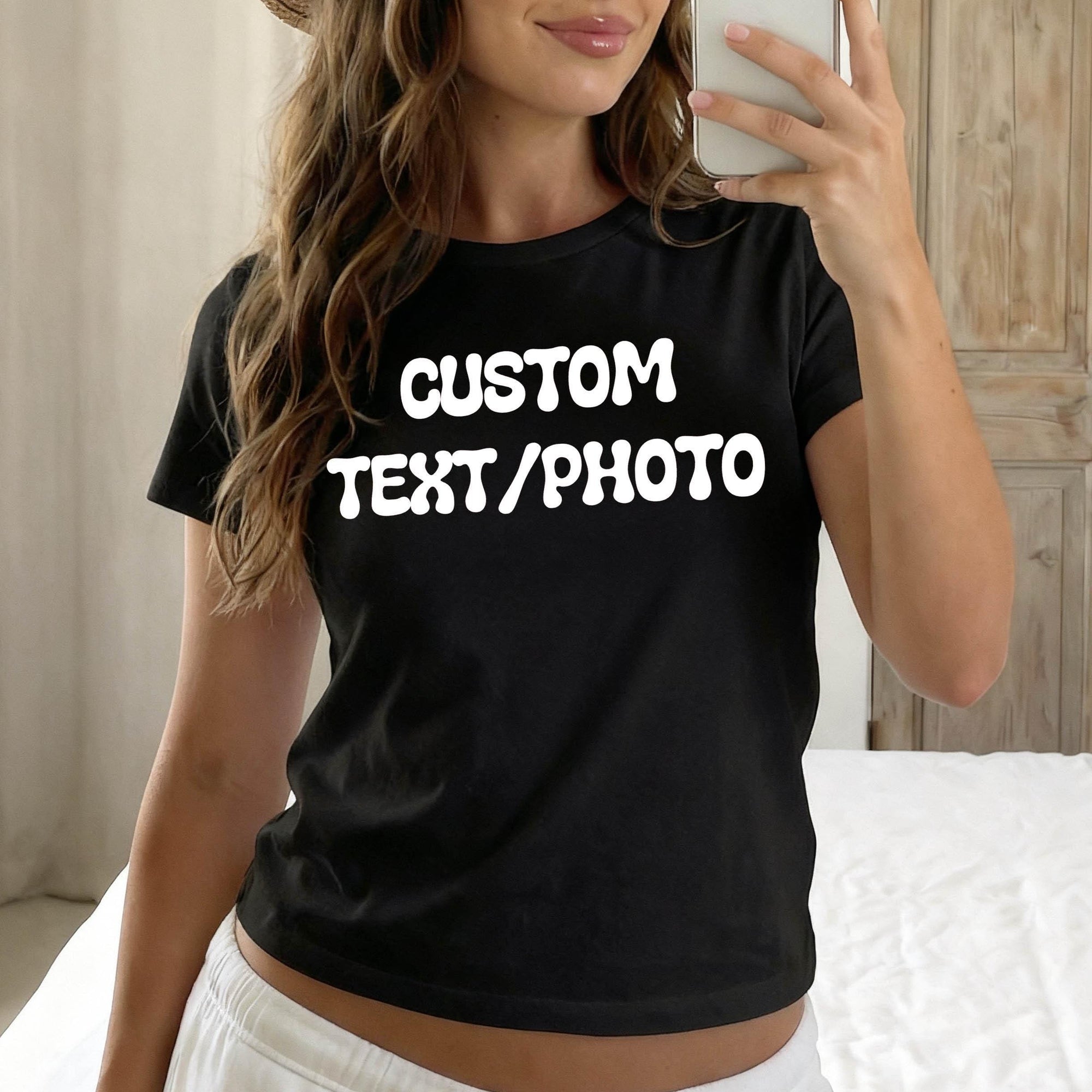 A woman wearing a black t-shirt with the text &amp;quot;CUSTOM TEXT/PHOTO&amp;quot; printed on it, taking a selfie with a smartphone.