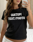 A woman wearing a black t-shirt with the text "CUSTOM TEXT/PHOTO" printed on it, taking a selfie with a smartphone.