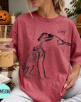 A woman wearing a red t-shirt with a skeleton drawing and the word "boop" printed on it, holding a glass of iced coffee.