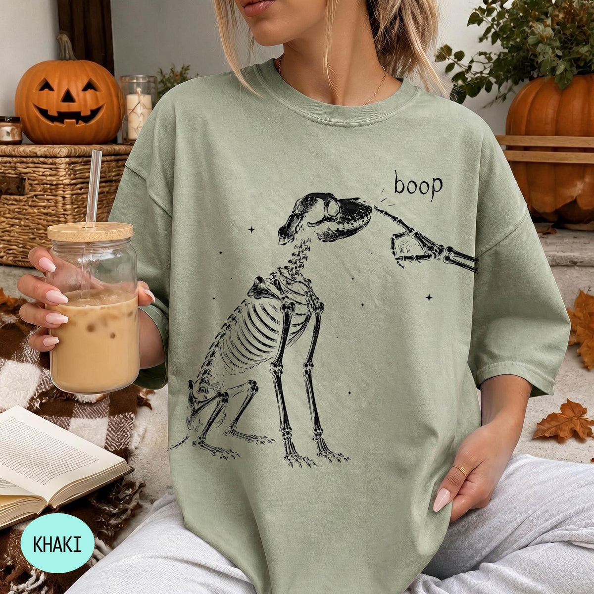 A woman wearing a green t-shirt with a skeleton graphic and the word &amp;quot;boop&amp;quot; printed on it, holding a glass of iced coffee.