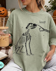 A woman wearing a green t-shirt with a skeleton graphic and the word "boop" printed on it, holding a glass of iced coffee.