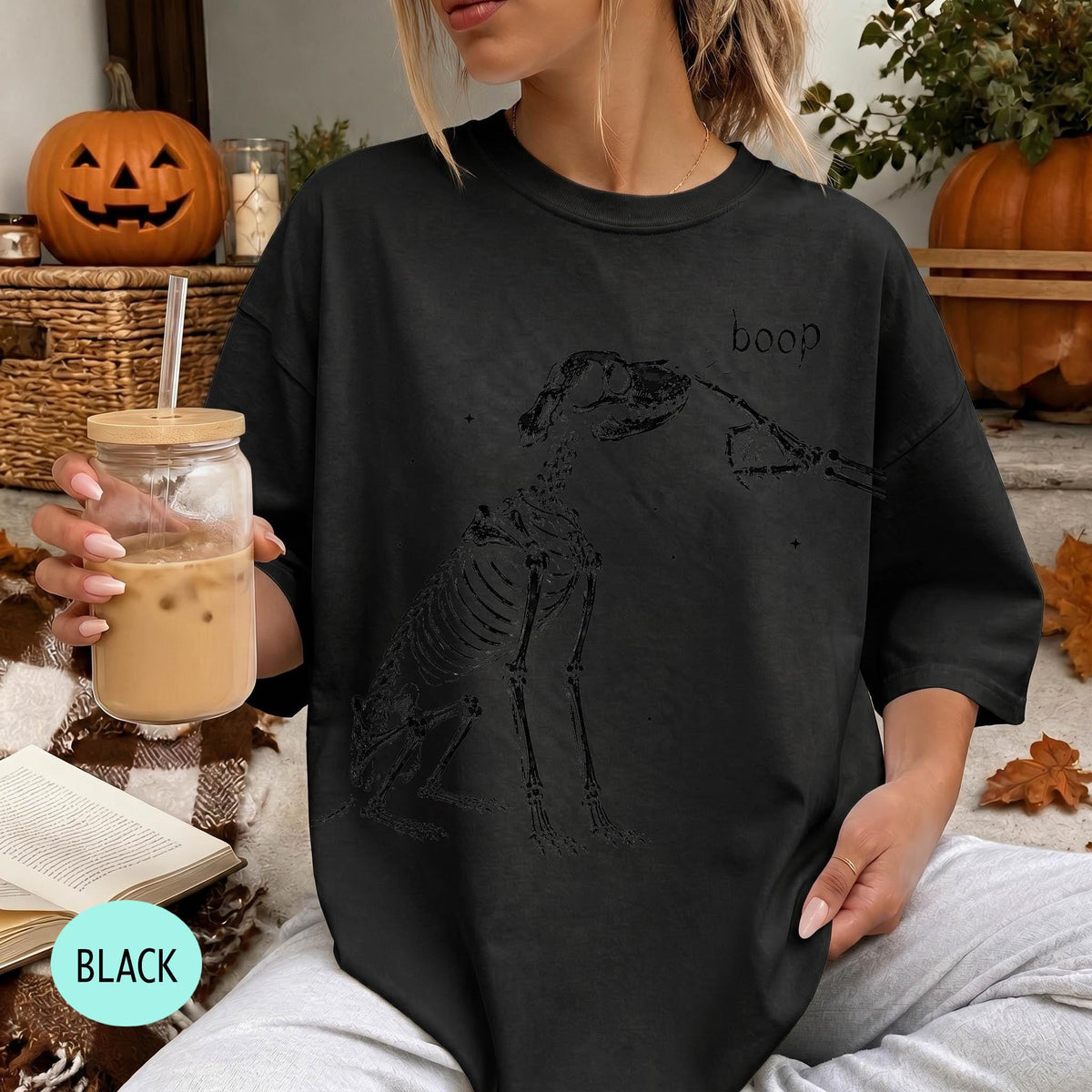 A woman wearing a black t-shirt with a skeleton drawing and the word &amp;quot;boop&amp;quot; printed on it, holding a drink in a glass.