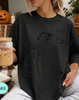 A woman wearing a black t-shirt with a skeleton drawing and the word "boop" printed on it, holding a drink in a glass.