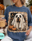 A woman wearing a blue t-shirt with a graphic of a ghost dog and pumpkins, holding a drink and surrounded by Halloween decorations.