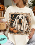 A woman wearing a white t-shirt with a graphic of a ghost dog and pumpkins, holding a glass of iced coffee.