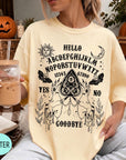 A woman wearing a yellow t-shirt with a Ouija board design and text printed on it, holding a drink in a glass.