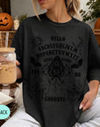 A woman wearing a black t-shirt with a Ouija board design and text printed on it, holding a drink in a glass.