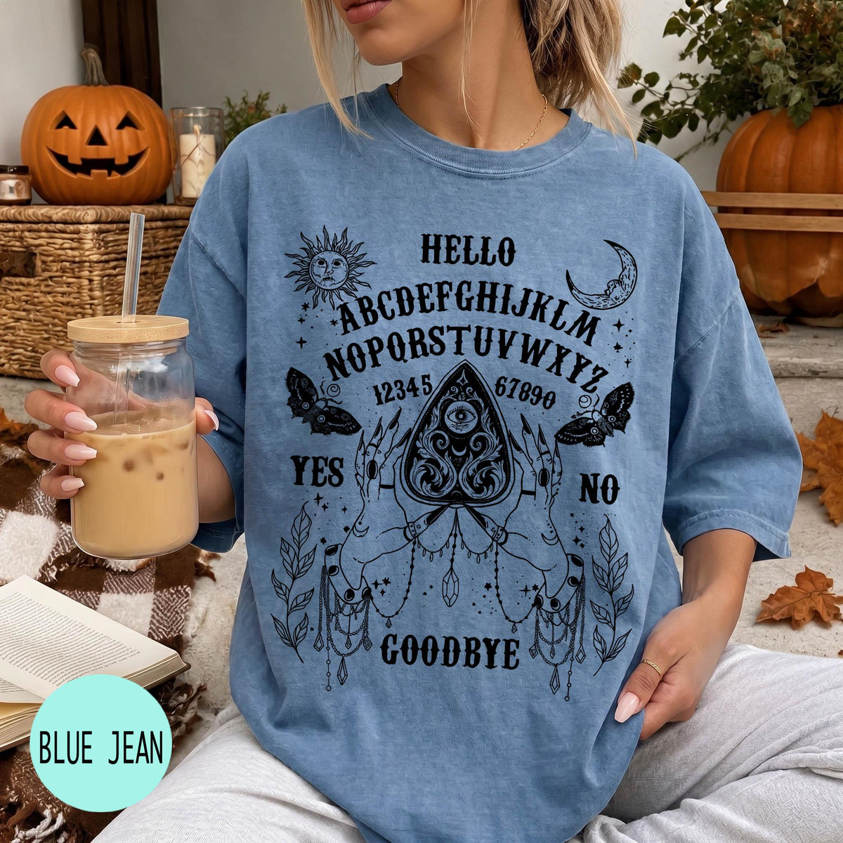 A woman wearing a blue t-shirt with a Ouija board design and text printed on it, holding a drink in a glass.