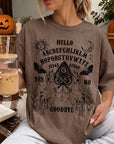 A woman wearing a t-shirt with an Ouija board design and holding a drink is sitting in a room decorated for Halloween.