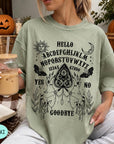 A woman wearing a green t-shirt with an Ouija board design and text printed on it, holding a drink in a glass.
