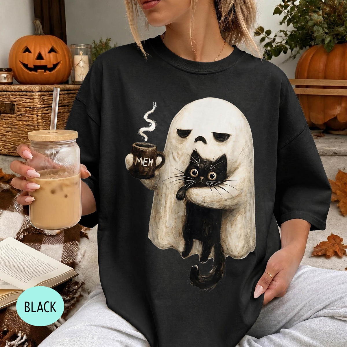 A woman wearing a black t-shirt with a graphic of a ghost holding a coffee mug and a black cat.