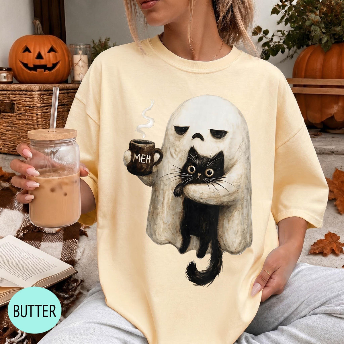 A woman wearing a yellow t-shirt with a graphic of a ghost holding a coffee mug and a black cat.